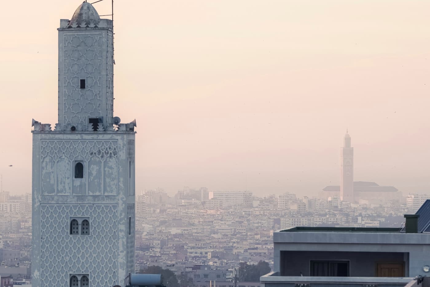 Toits de Casablanca et minaret au crépuscule, avec la Mosquée Hassan II en arrière-plan